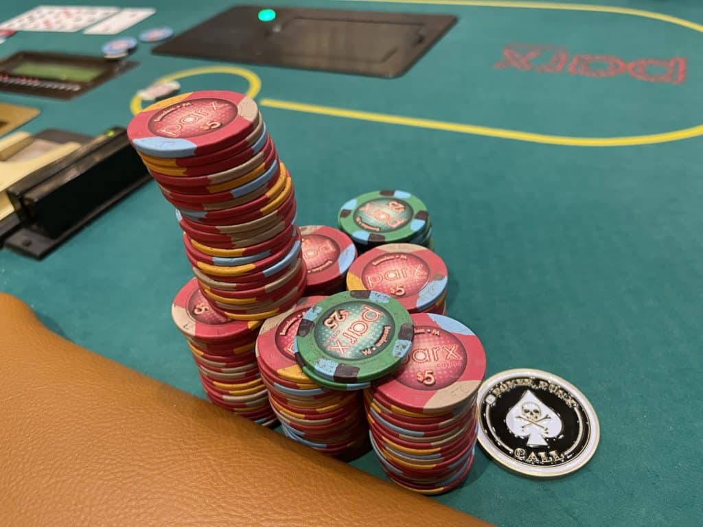 Poker chips stacked high on a green poker table with a skull-themed chip nearby.